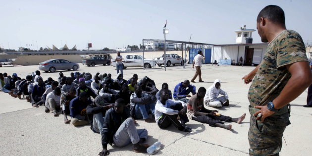 Member of Libya's Navy stands near illegal immigrants who tried to flee the coast to Europe after they were detained at Libyan's navy base in the the coastal city of Tripoli